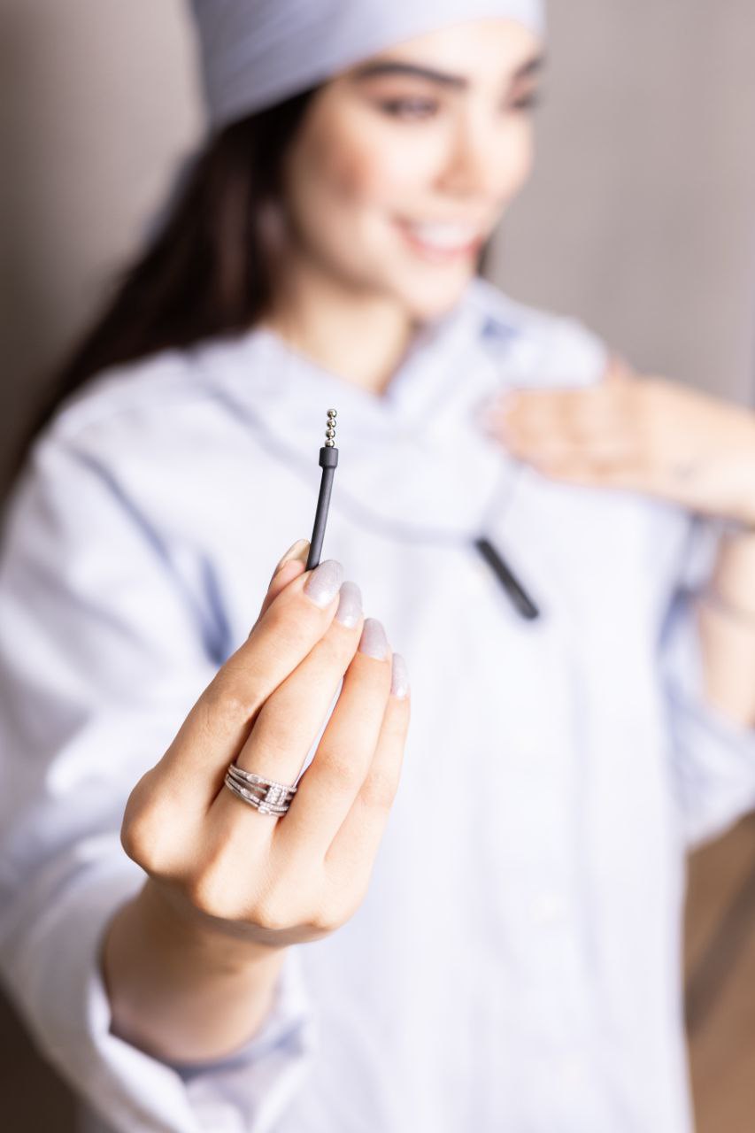 Woman holding slim insertion tube for 2 mm bead earpiece, with Croco neck unit blurred in background.