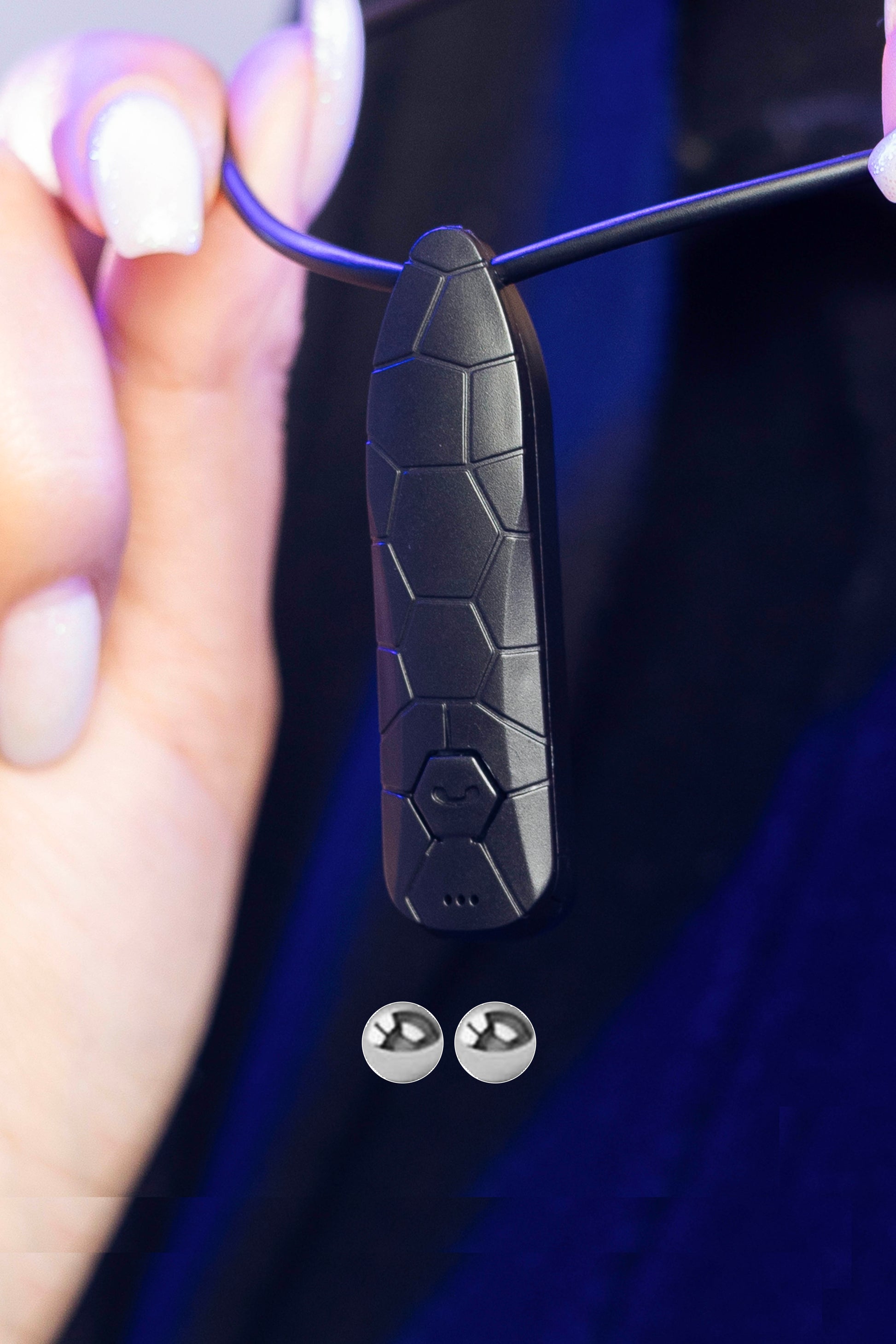 Close-up of Invisi2 Croco neck receiver held by hand, with two 2 mm bead earpieces shown below on dark background