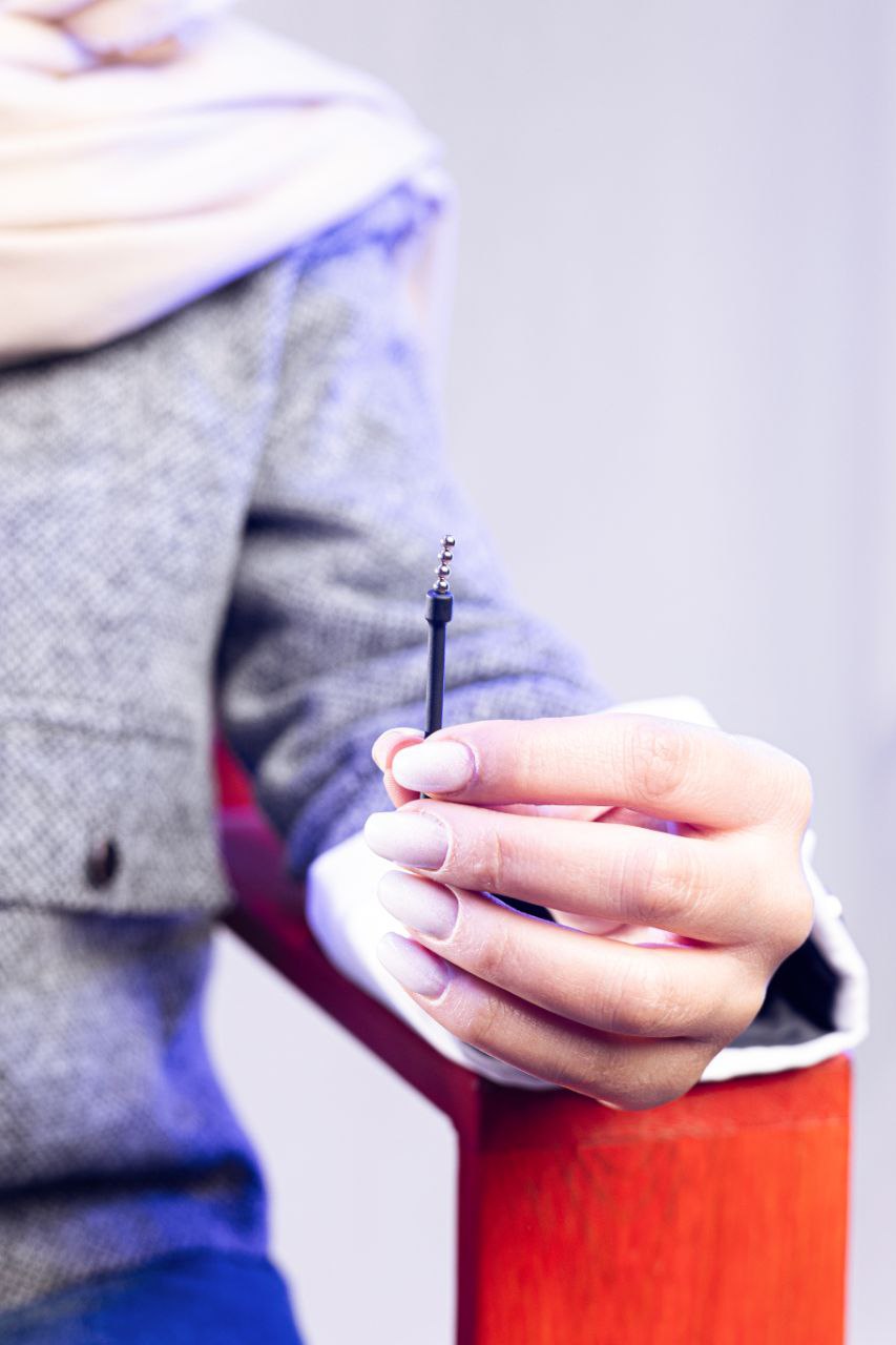 Woman holding slim black insertion tube with stacked 2 mm bead earpieces, focus on hand and tool.