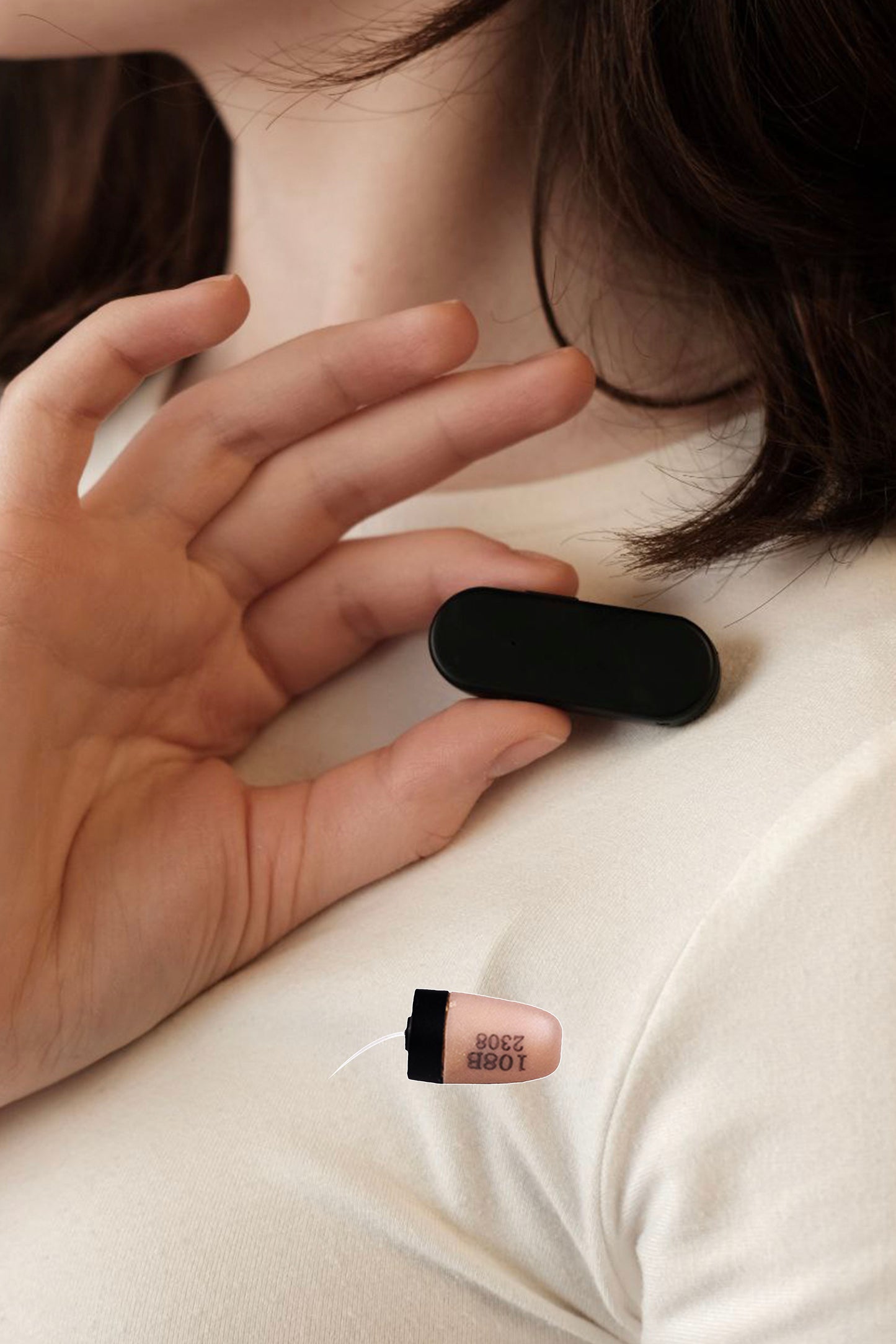 Hand placing Invisi2 Magic black wireless receiver on chest, with separate 4 mm capsule earpiece for scale.







