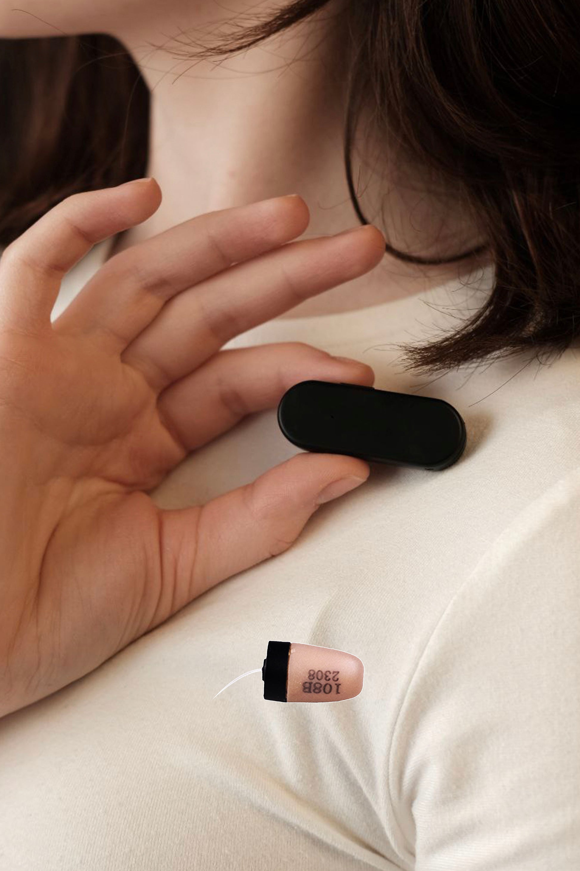 Hand placing Invisi2 Magic black wireless receiver on chest, with separate 4 mm capsule earpiece for scale.







